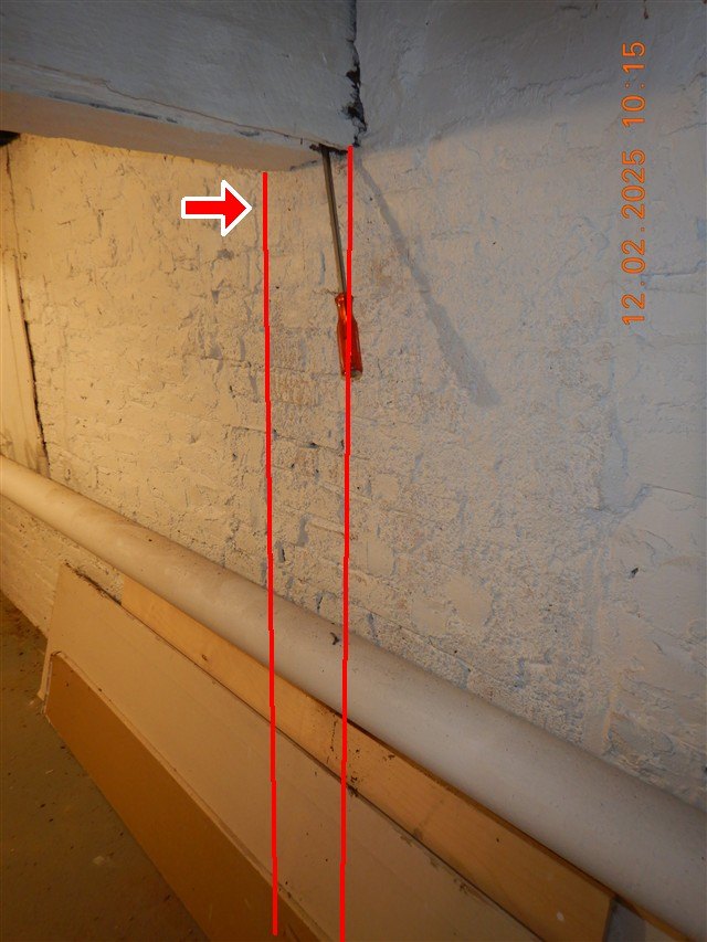 Screwdriver stuck into a wood beam above a painted brick basement wall, with a crack traced in red lines