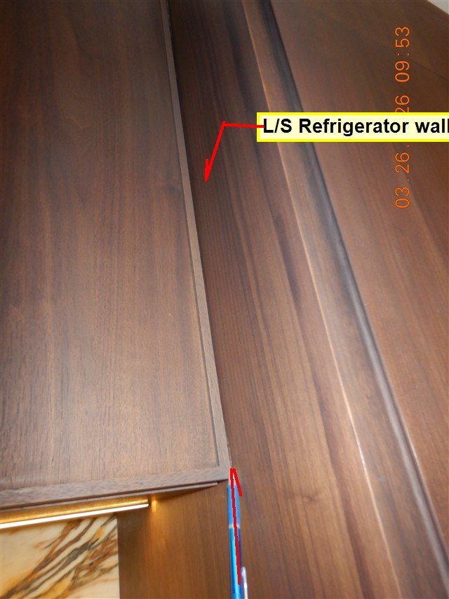 Dark wood cabinet door beside a refrigerator cabinet wall, with a yellow label and red arrows marking where the door hits
