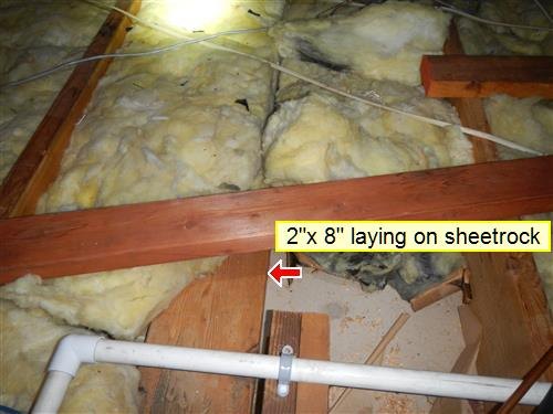Attic with fiberglass insulation between joists and a loose 2x8 ceiling joist laying on the sheetrock, red arrow