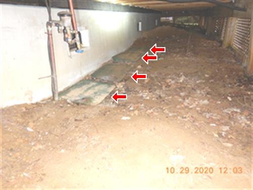 Dirt floor under a rear deck with red arrows marking green lawn irrigation control box lids along the wall