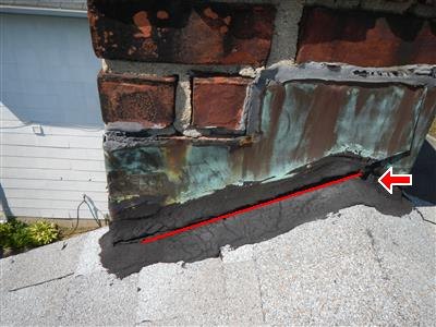 Brick chimney at roofline with green-patinated metal flashing and black tar patching, red line and arrow