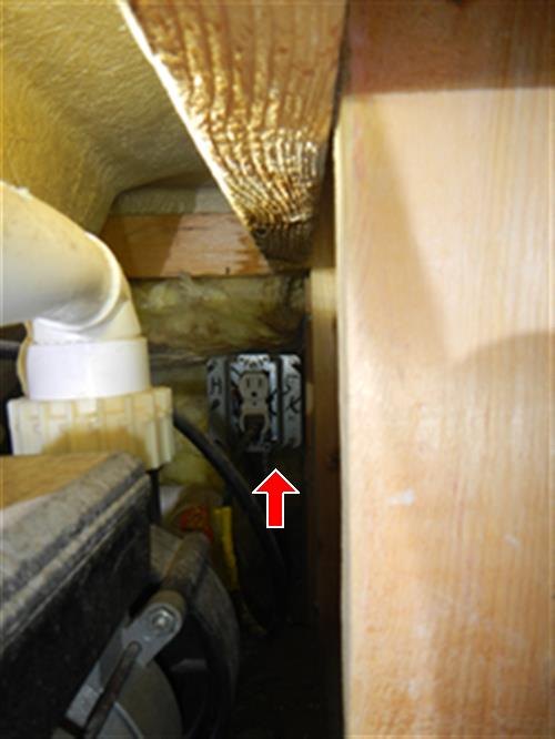 Red arrow pointing to an electrical outlet in the access space under a tub, beside a white drain pipe