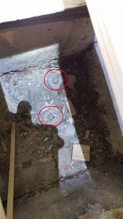 Two red circles around capped pipe fittings in a debris-filled pit under a floor opening