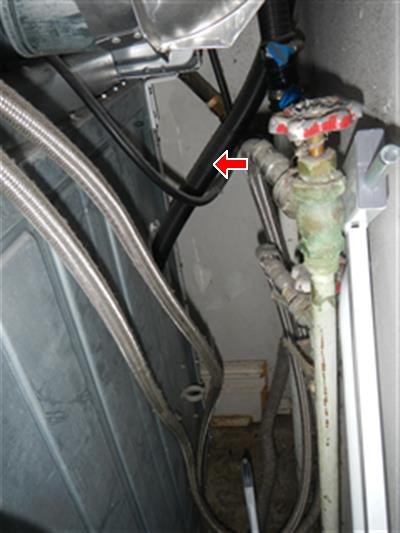 Red arrow marking a black rubber hose behind a clothes washer, beside a corroded shutoff valve