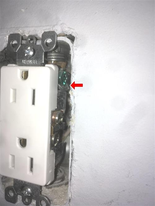 Electrical outlet pulled from a wall opening, red arrow at the green grounding screw