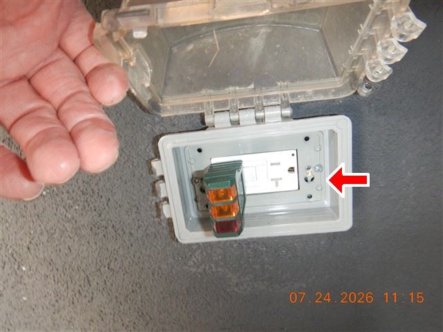 A plug-in receptacle tester held against an outlet during an inspection, its indicator lights showing the wiring condition.