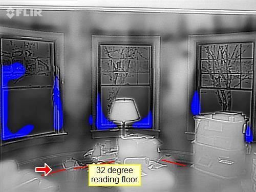 Thermal camera image of a room, with cold areas showing blue beneath three windows and a marked 32 degree reading at floor level.