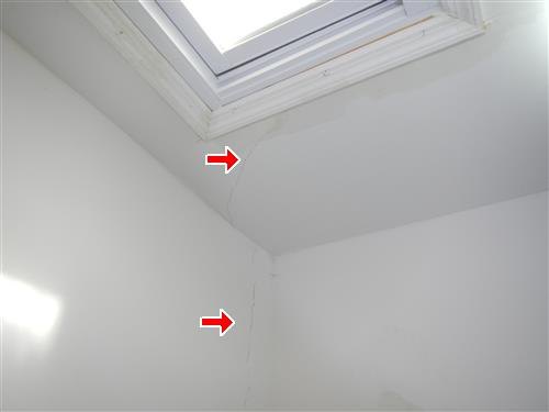 A skylight well in a sloped ceiling with a crack marked by red arrows where it runs into the wall.