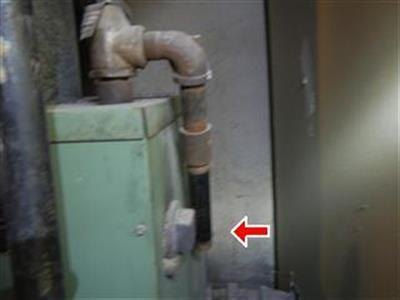Older green boiler with a red arrow at the end of its relief-valve extension pipe.
