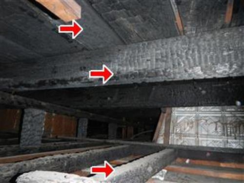 Charred roof rafters and a beam viewed from below, three red arrows at burned areas.