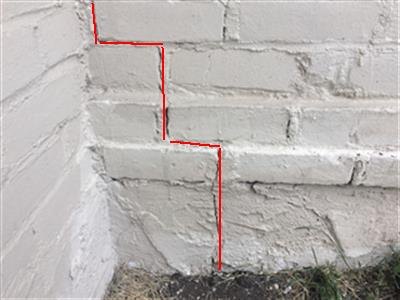 The painted brick base of a chimney with a step crack traced in red.