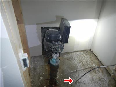 A water meter at the service entry with a red arrow marking a broken ground wire on the floor.