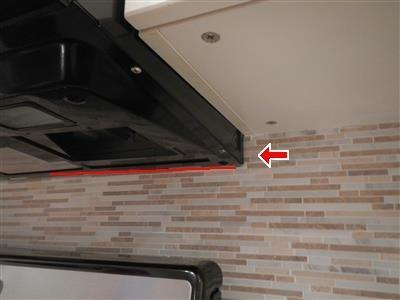 Underside of a black over-the-range microwave against a tiled backsplash, with a red line and arrow markup.