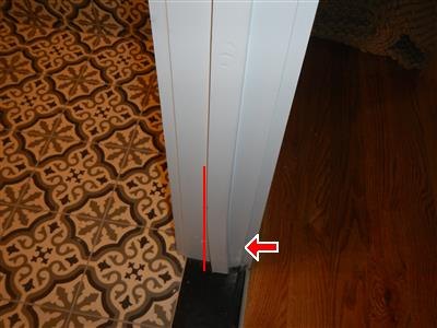 White door frame with a red line tracing the door stop strip and an arrow at the loose piece at its base, between tile and wood floors.