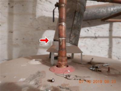 Copper pipe rising from a water heater top with a flue pipe behind it, red arrow at the contact point, orange date stamp.