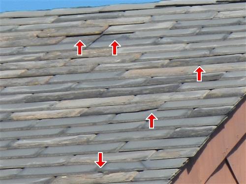 A slate roof with several missing, broken or slipped pieces marked by red arrows.