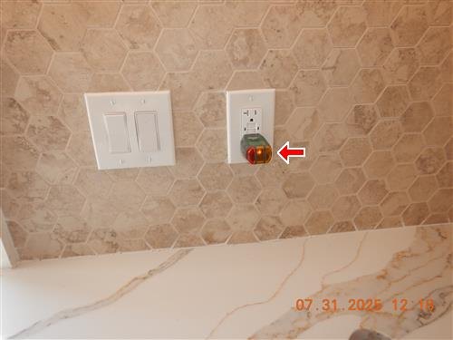 A kitchen backsplash with an outlet tester plugged into a GFCI receptacle, marked by a red arrow.
