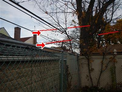 Low overhead cable wires crossing a yard above a chain-link fence, traced with red lines and two arrows.