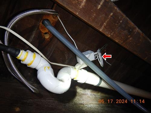 Basement ceiling with drain piping, flexible hoses, and a red arrow at a plug-in cord connection.