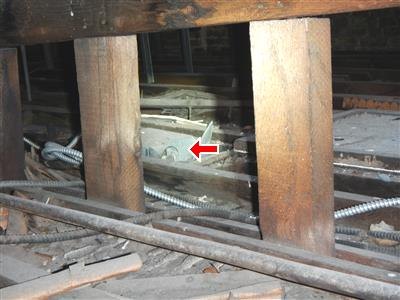 Dark framed space with wood posts and armored cable runs, red arrow at a bath exhaust fan housing among the framing.