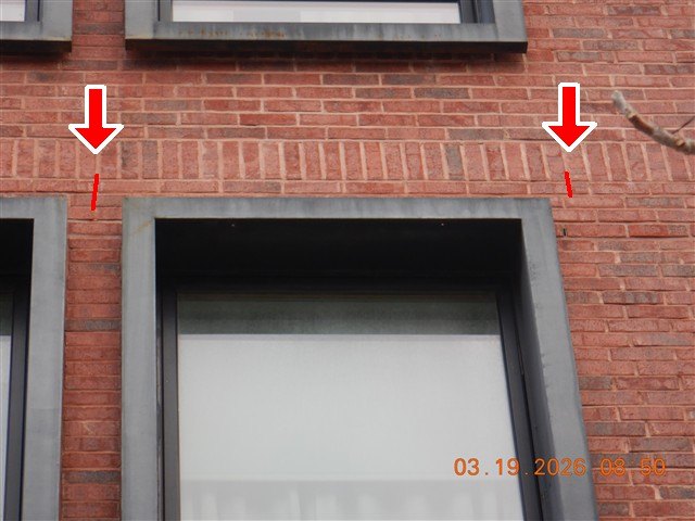 A newer red-brick facade with red arrows marking the bed joints beside dark metal window surrounds.