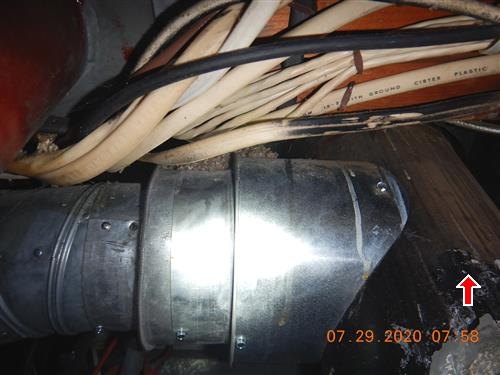 Bundle of wires draped over a large metal flue pipe in a dark utility closet, red arrow at lower right