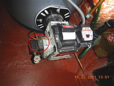 Oil burner mounted on an oil-fired water heater, red circle around the fuel shut-off solenoid, orange date stamp