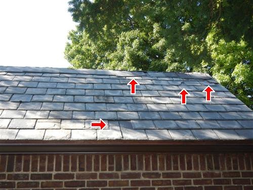 An older grey slate roof with red arrows marking missing and loose slates and a darker repaired area