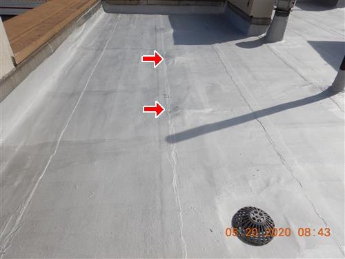 Silver-coated flat roof with a domed drain strainer, two red arrows at raised spots along a seam, orange date stamp