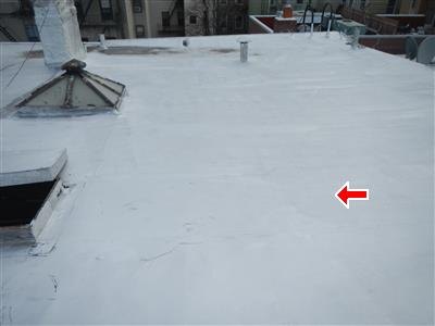 Silver-coated flat roof with a skylight vent and a pipe penetration, red arrow at a seam line