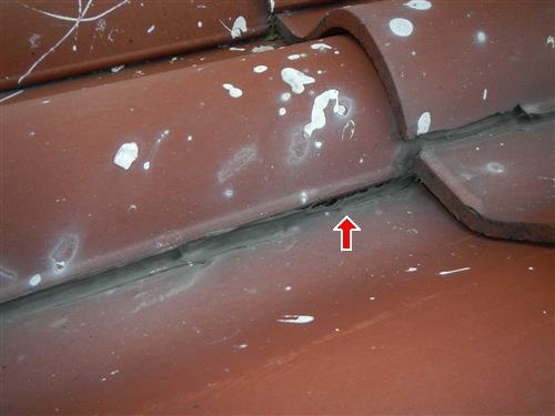 Terracotta clay roof tiles with old silicone sealer along the joints, one joint arrowed
