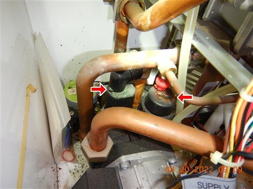 Copper pipes and two corroded components on the left side of a heat boiler, marked by red arrows
