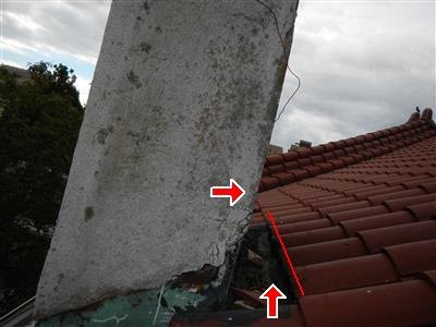 Red arrows at the cracked, broken edge where a stucco chimney meets a clay tile roof
