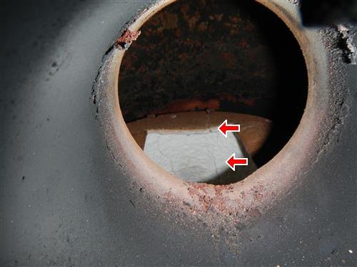 View through a round furnace inspection port at the firebox inside, with red arrows marking a crack.