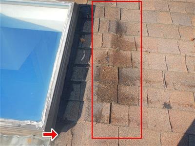 Asphalt shingle roof beside a skylight with a red box marking buckling shingles and an arrow at a metal deflector piece