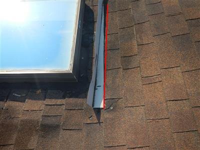 A loose piece of metal flashing beside a skylight on an asphalt shingle roof, with a red line along its raised edge