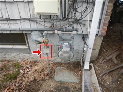 Exterior gas meter and regulator on a house wall, with the main gas shut-off valve boxed in red