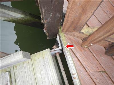 Timber dock and ramp meeting at the waterline, with a red arrow at a loose hinge support