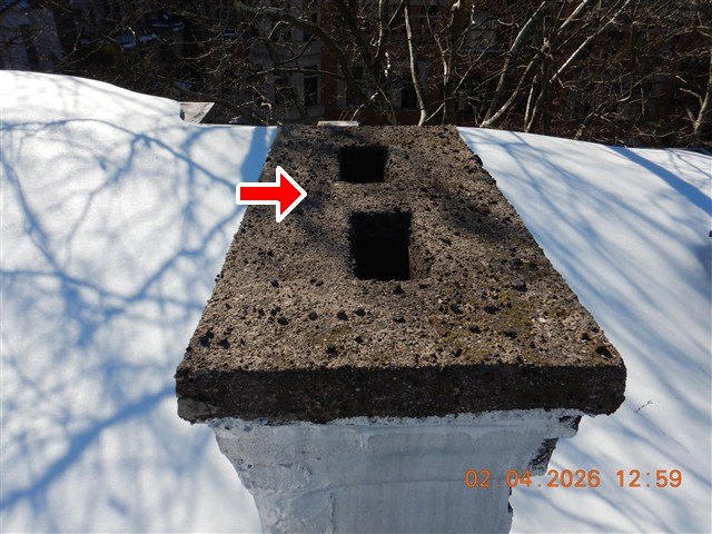 An old masonry chimney with two open square flues on a snow-covered flat roof, red arrow at the crown
