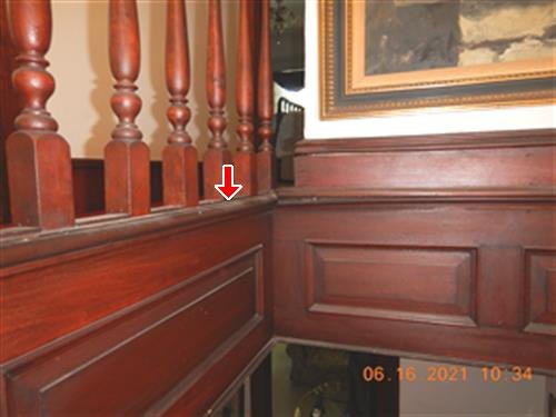 Dark wood hallway balustrade and raised paneling with a red arrow where the railing meets the wall