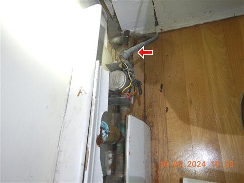 Zone valve and older piping in a floor opening beside a cabinet, red arrow at an armored cable connector