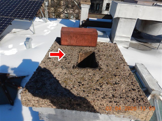 Rooftop chimney cap with an open flue hole and a brick resting on top, red arrow, snow around