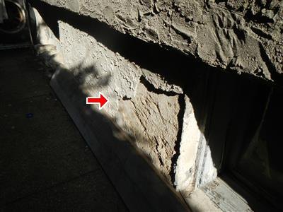 Stucco broken loose at the base of a wall where it meets the foundation, red arrow at the damage