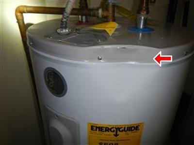 Top of an electric water heater with copper piping, red arrow at a dented case rim