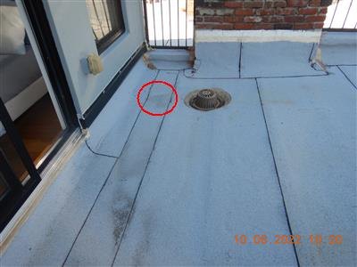 Silver-coated flat roof with a metal drain strainer near a sliding door; a red circle marks a low spot between the drain and the wall