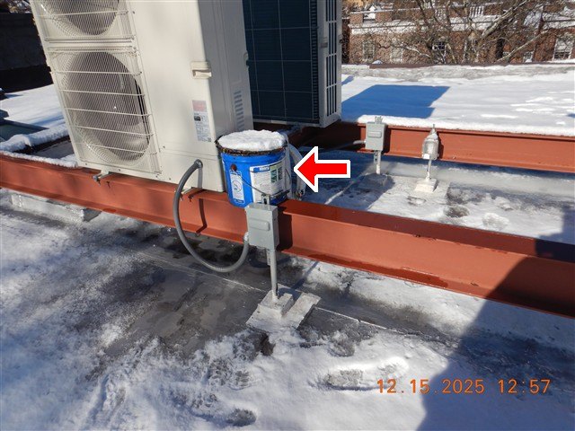 Snow-covered flat roof with two condenser units on steel rails and a red arrow at an old roofing-cement can left on the roof