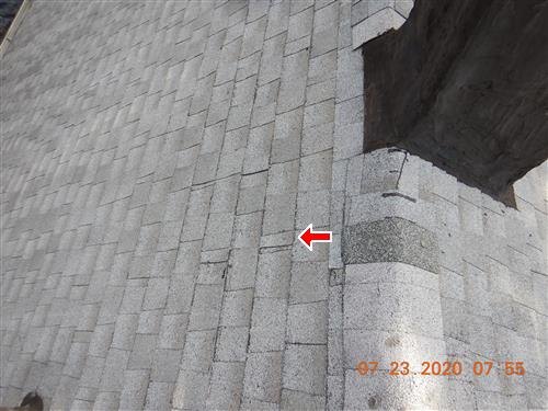 Light-coloured roof shingles beside a chimney, with a red arrow marking a worn area.