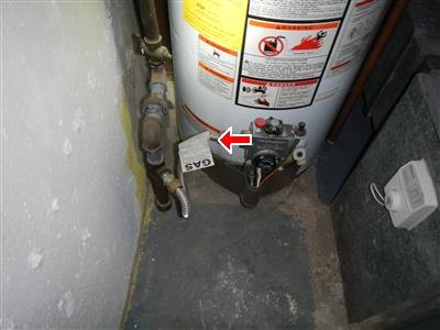 A gas water heater in a tight corner, with a red arrow at its gas piping connection.