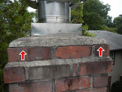Brick chimney top with a metal flue pipe, red arrows pointing at the cracked concrete cap.