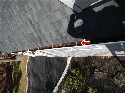 Looking down a roof edge at a gutter filled with debris, a red arrow pointing at it.